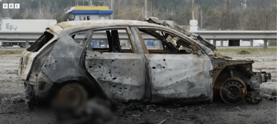 A burnt car can be seen near the road