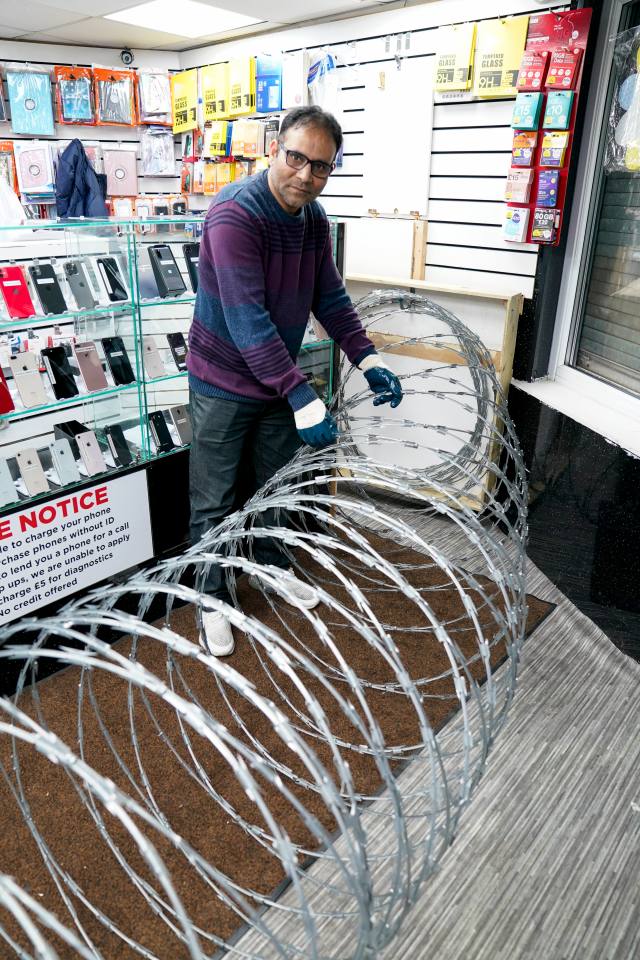 Parvez Akhtar rolls out razor wire to protect his mobile phone shop in Parliament Road, Middlesbrough