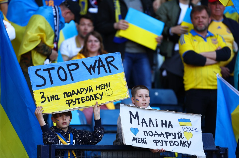 Ukranian fans hold up signs begging for an end to the war in their country