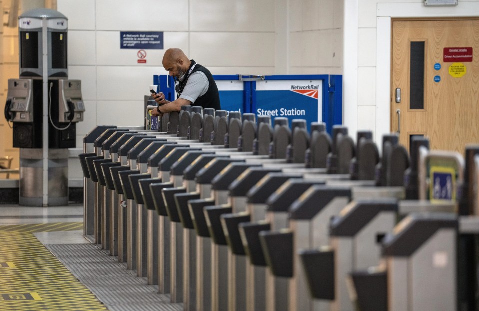 A railway worker checks his phone as he waits by ticket gates at Liverpool Street train station