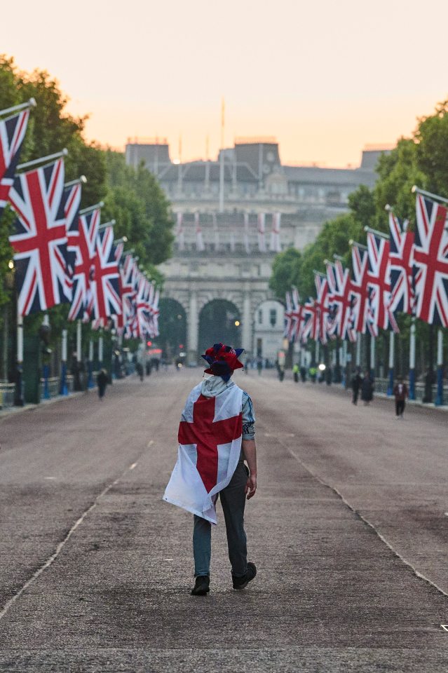 A man draped in an England flag walks down The Mall at sunrise