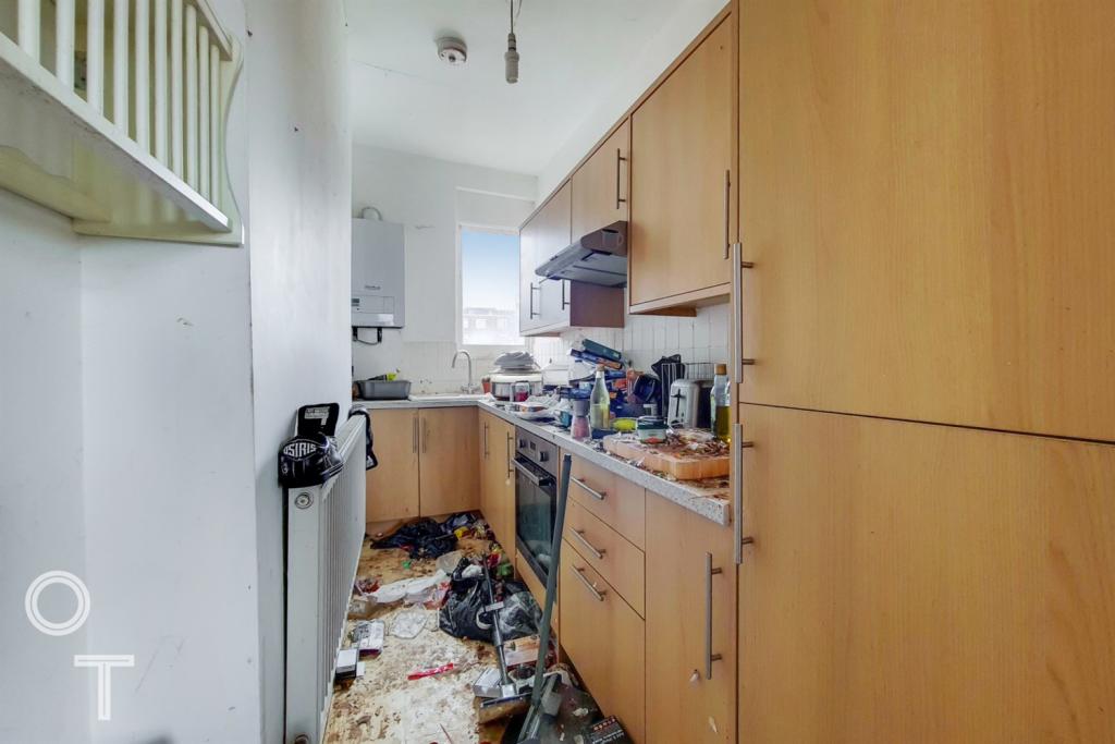 A previous tenant has left the apartment in a bad state. The kitchen is particularly grim, with black bags dumped on the laminate and cardboard boxes piling up beneath a cupboard