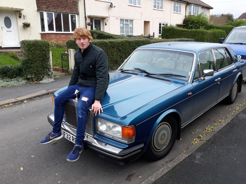 a man sits on the hood of a blue car with a license plate that says f82 rf