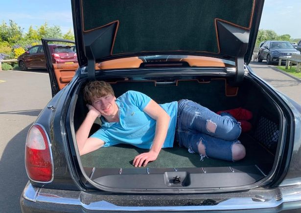 a young man is laying in the trunk of a car