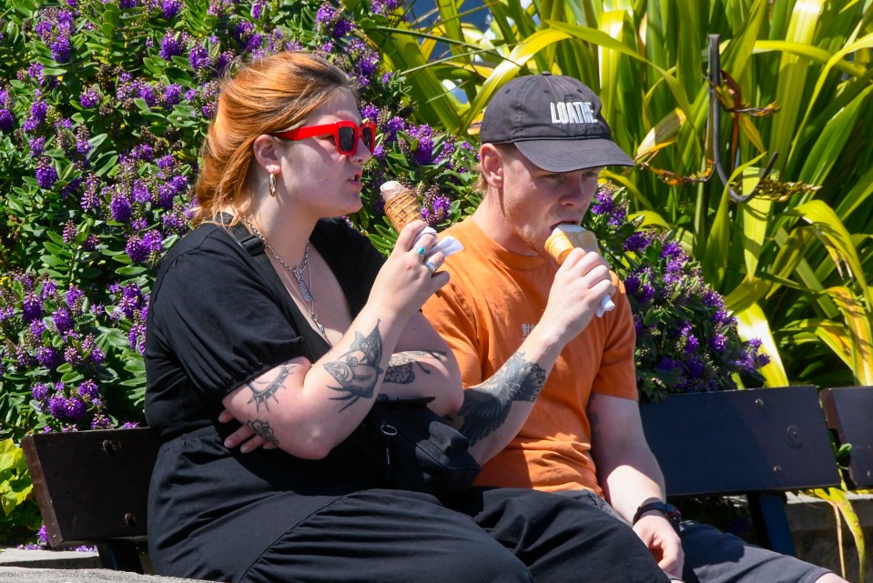 A couple sitting on the seafront enjoying an ice cream in the scorching hot sunshine