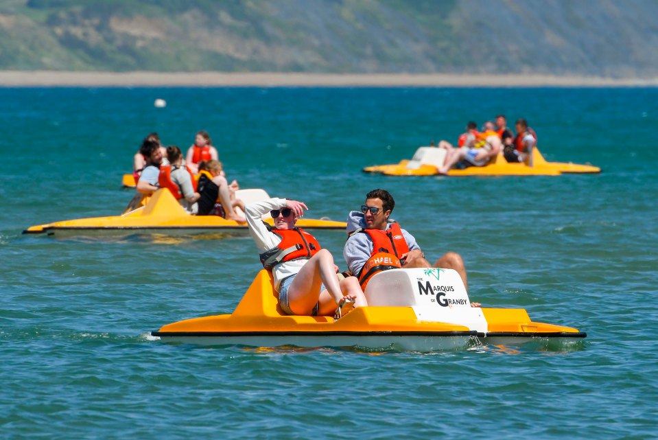 Beachgoers having fun on pedalos on the calm sea in the sunshine at the seaside resort of Weymouth