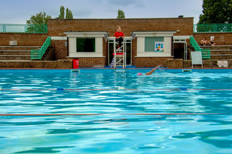 a lifeguard sits on a ladder overlooking a swimming pool