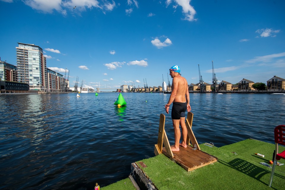 a man in a blue swim cap stands on a dock overlooking a body of water