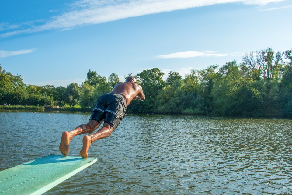 a man is jumping into a lake from a diving board