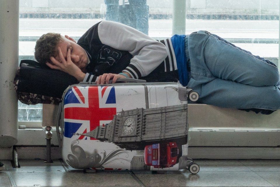 A tired passenger lays down with his head in his hands as he waits for a flight at Stansted