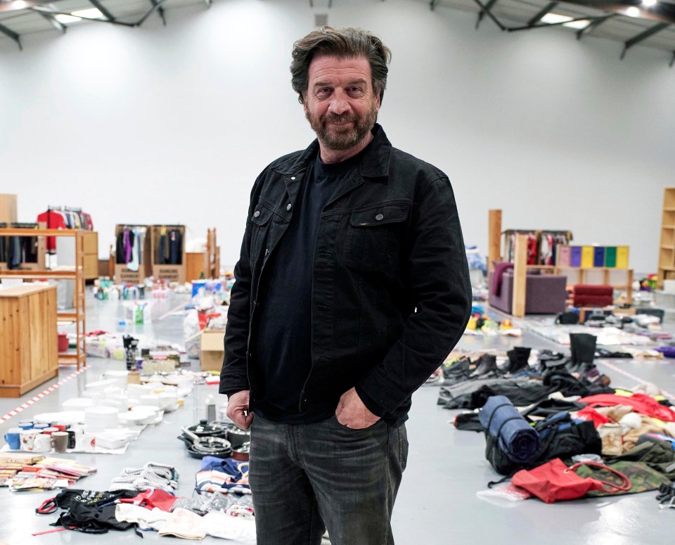 a man in a black jacket stands in a messy room