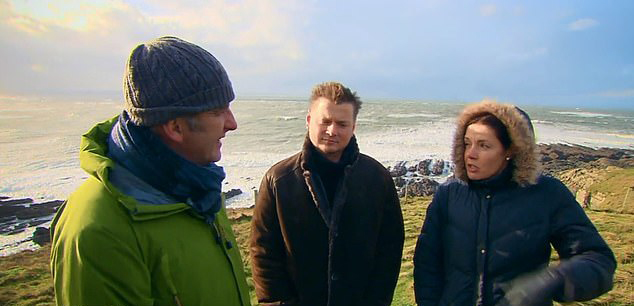 a man and a woman are standing next to each other on a hill near the ocean .