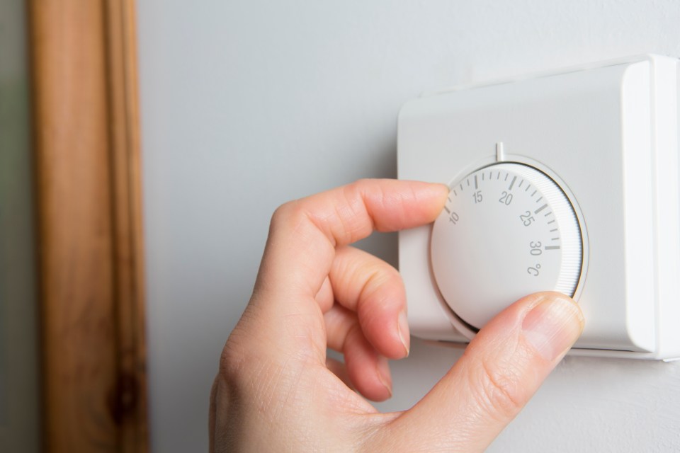 Close Up Of Female Hand On Central Heating Thermostat