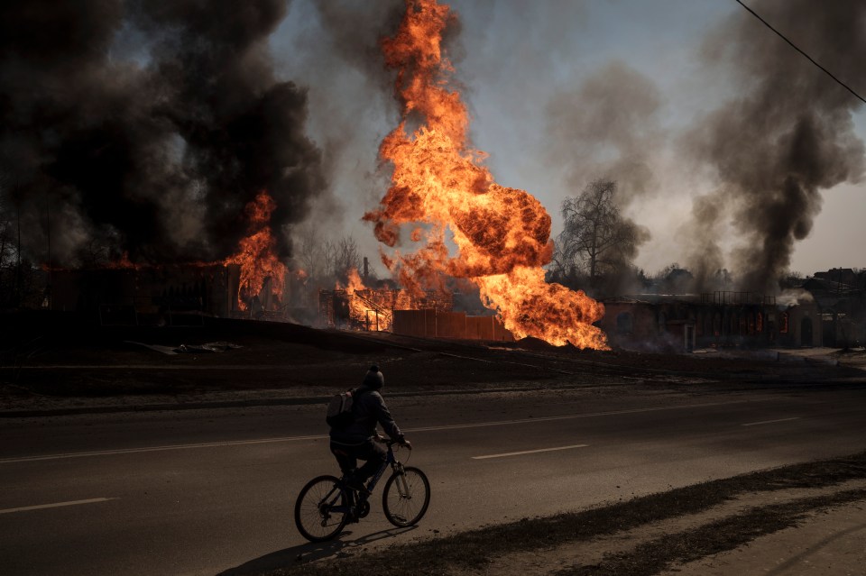 A man rides his bike as flames rise following a Russian attack in Kharkiv, Ukraine, on March 22 this year