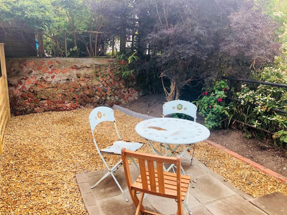 Beyond the door lies a wood-chipped garden with a table and chairs