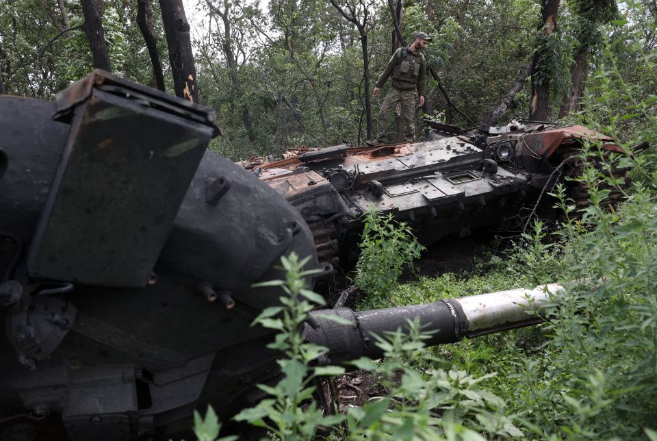 A Ukrainian soldier stands on a destroyed Russian tank near the front line in Kharkiv region