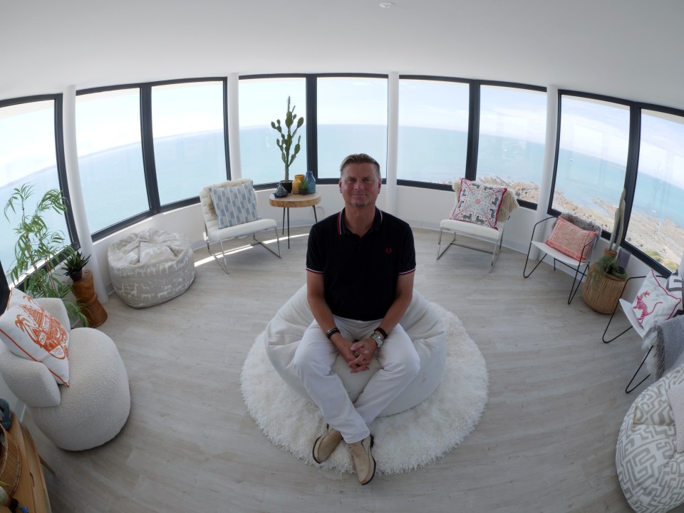 a man sits on a bean bag chair in a room with a view of the ocean