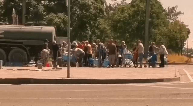 Families queue to fill up a few water bottles and buckets coming from a truck