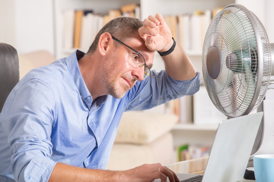 Man suffers from heat while working in the office and tries to cool off by the fan