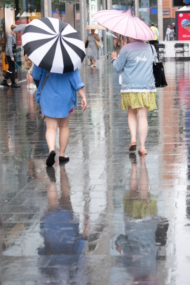 Shoppers shelter from the rain under umbrellas