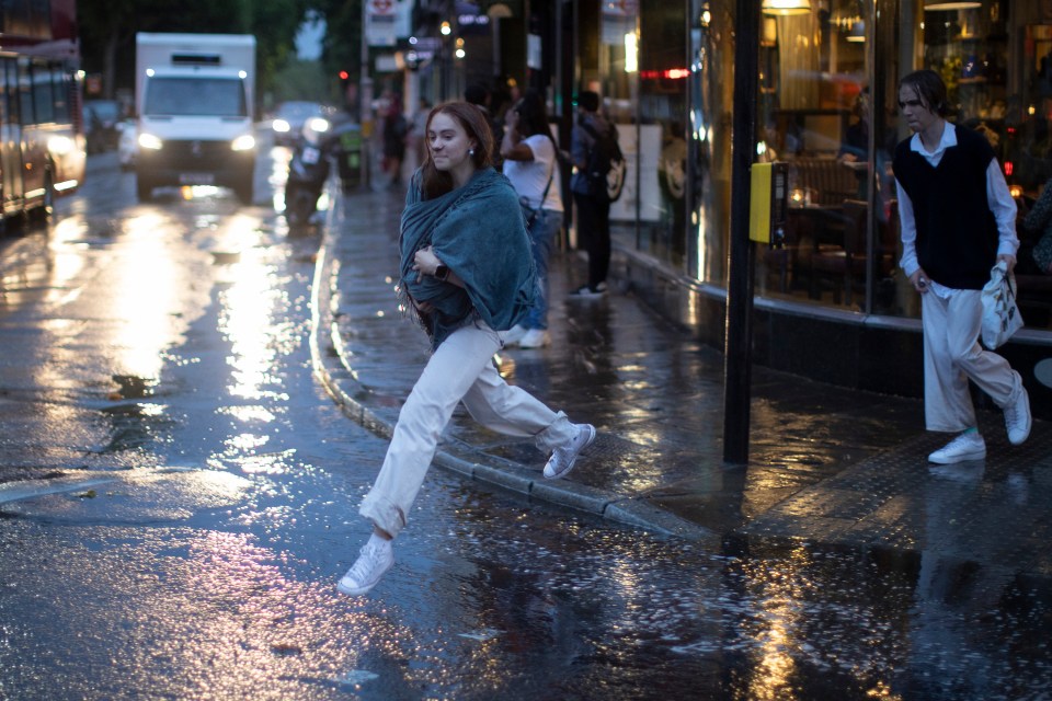 A woman attempts to jump over a puddle during heavy rain in Greenwich, London