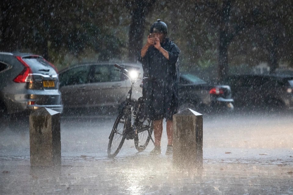 A man attempts to snap a photo during heavy rain in London today