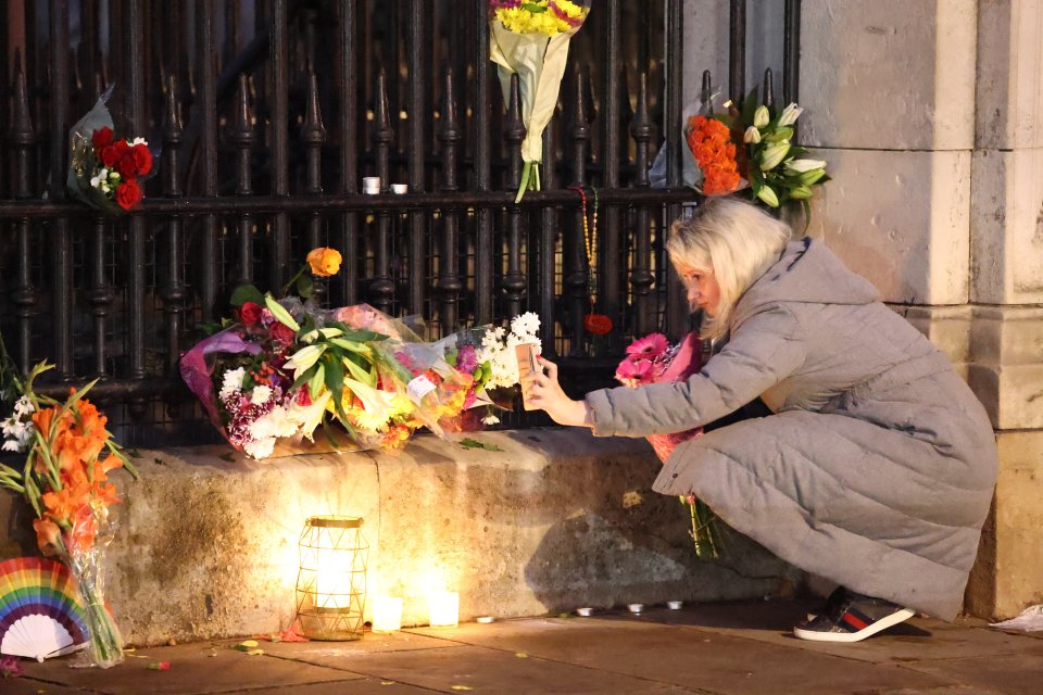 A woman takes photos of flowers outside Buckingham Palace