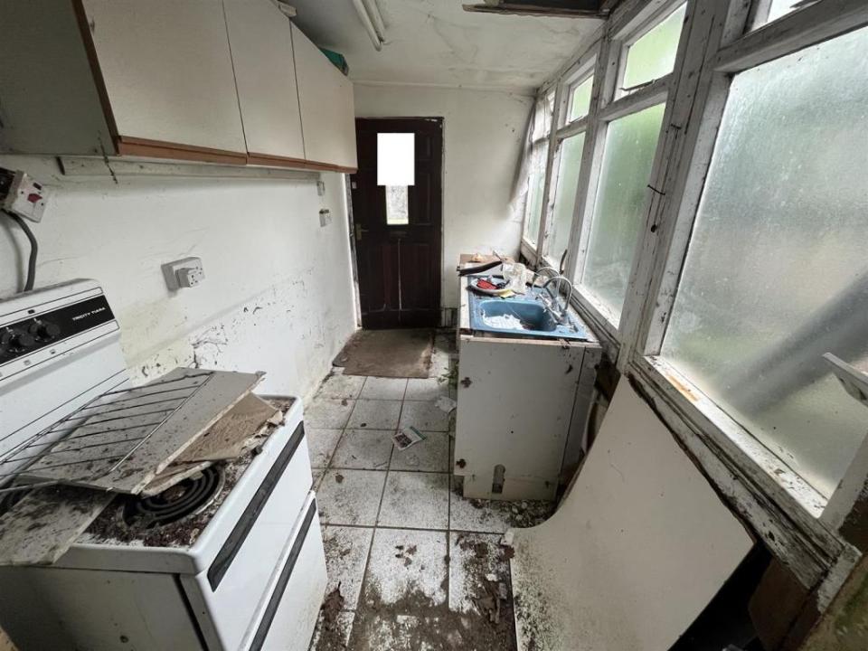 Kitchen cupboards are missing, the oven is covered in dirt and plasterboard and the floor is dirty