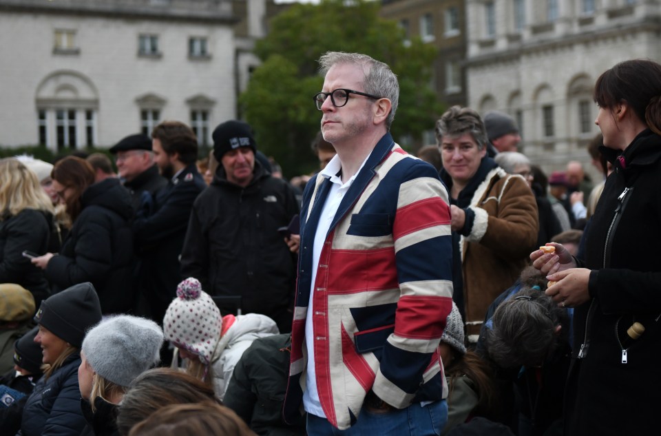 A mourner wearing a Union Jack flag jacket waits with others at Horse Guards