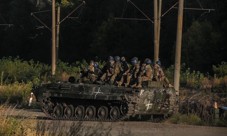 Ukrainian army fighters sit on the top of an armed vehicle in Kharkiv