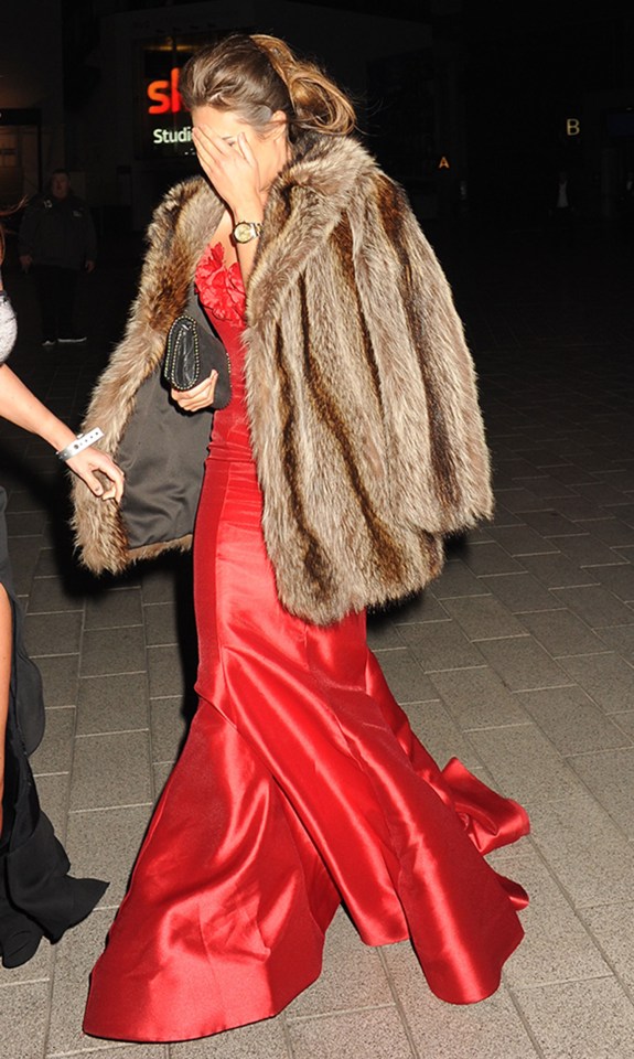 a woman in a red dress covering her face with a fur coat