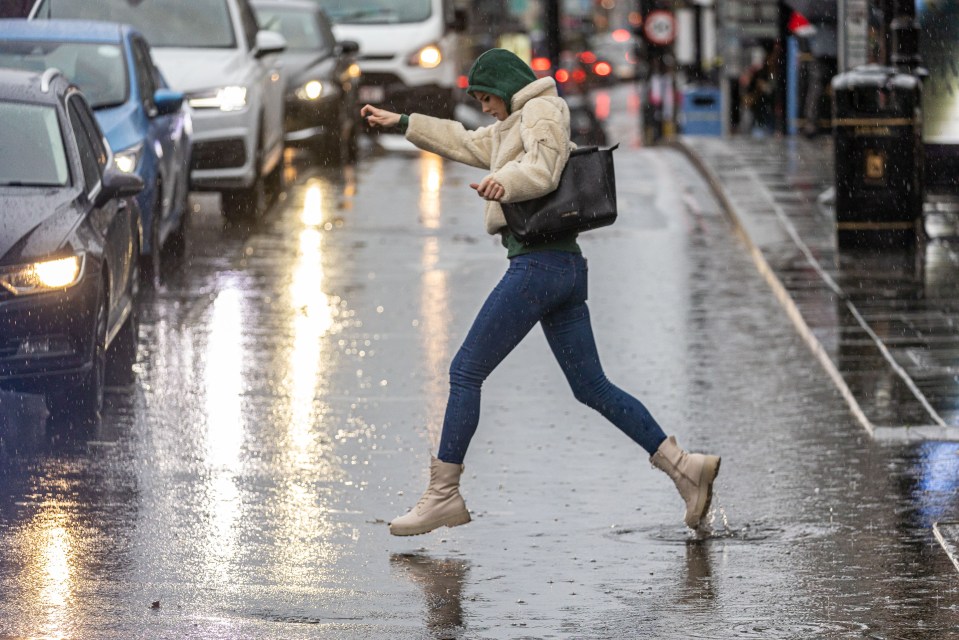 A woman leaps across a puddle on Putney High Street, South West London