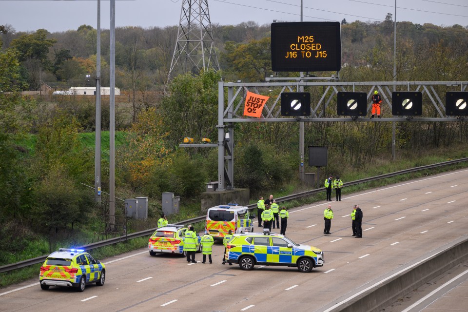 Police officers attempt to stop an activist as they put up a banner reading "Just Stop Oil" atop an electronic traffic sign along M25 on November 10, 2022