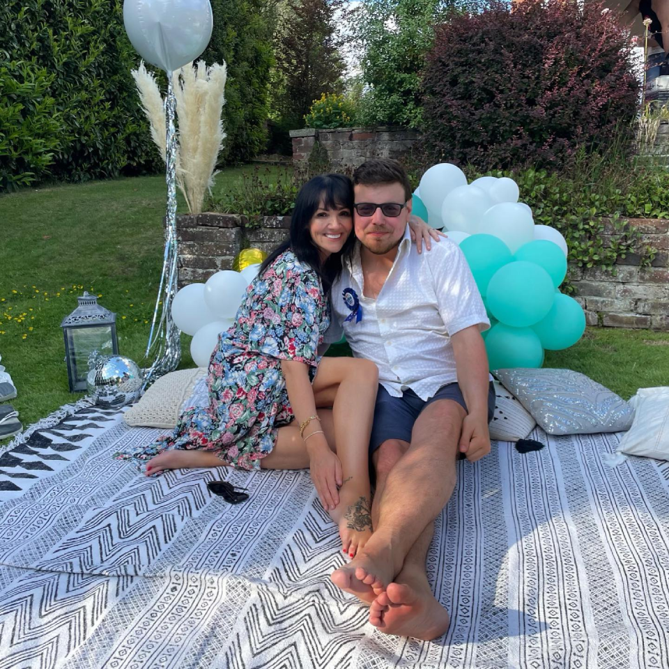 a man and woman sitting on a blanket with balloons in the background