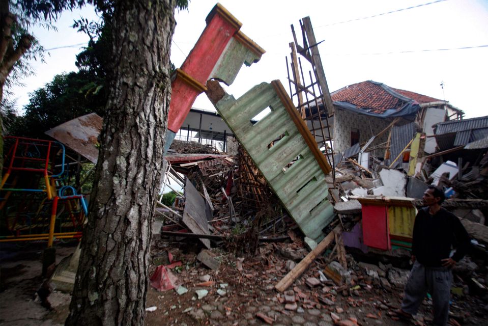 A man stands beside damaged houses