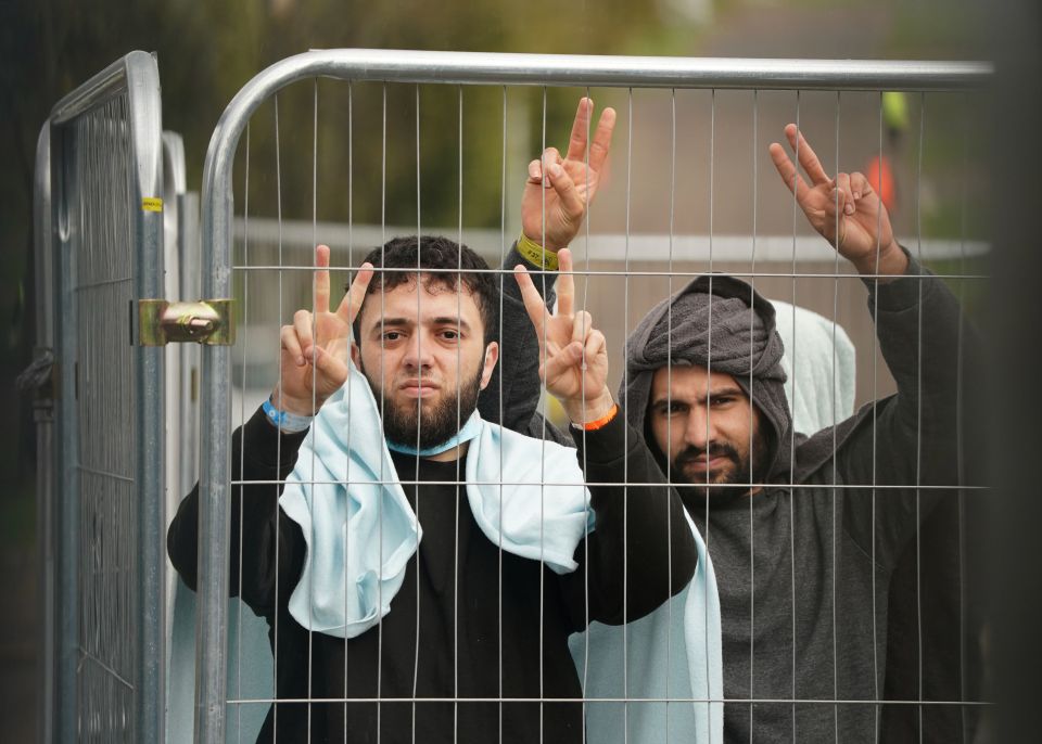 Migrants gesture through barriers at the Manston immigration centre in Thanet, Kent