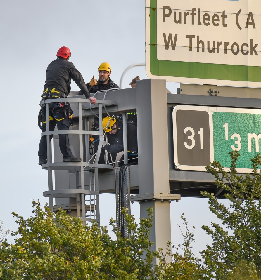 Police move in to remove a Stop Oil protester on an M25 gantry near to Junction 31