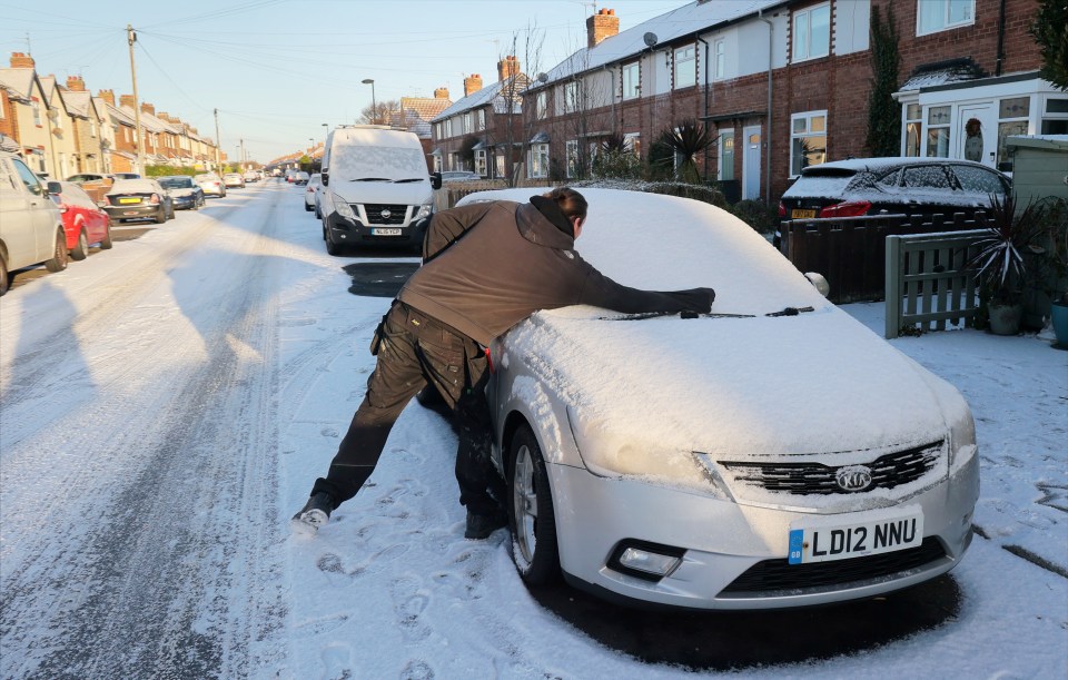 A driver clears snow from their windscreen after another icy day