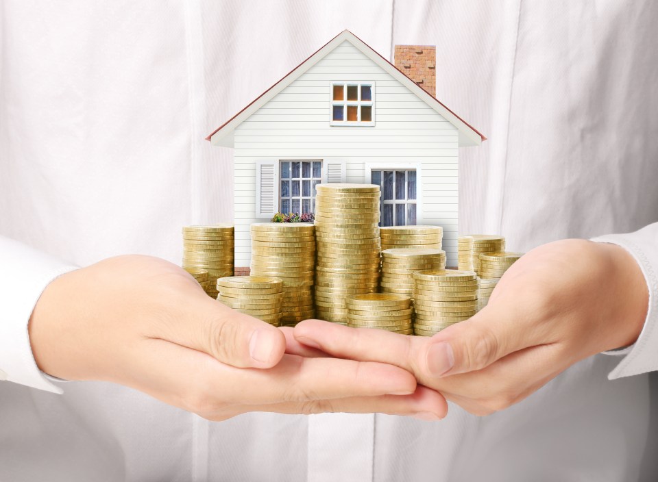 a person holding stacks of gold coins in front of a house