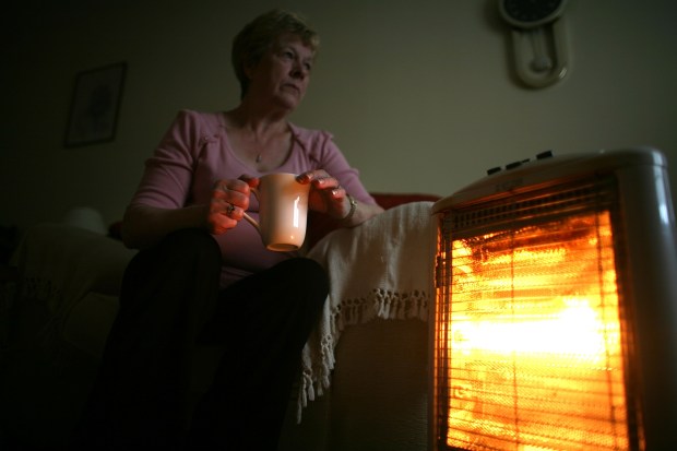 a woman sits in front of a heater holding a cup of coffee