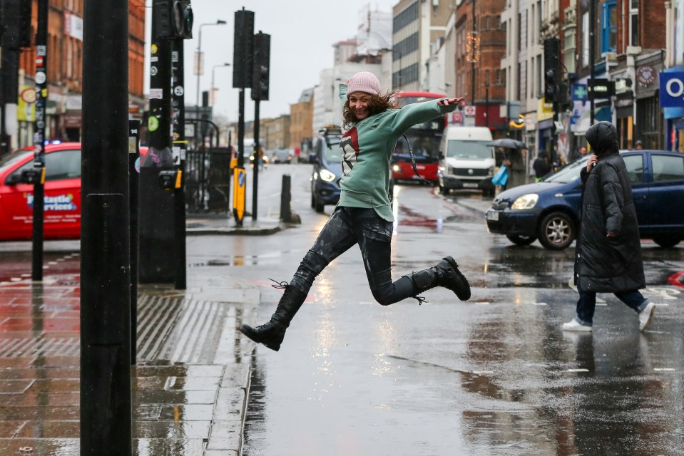 A woman leaps over a large puddle in Camden, North London