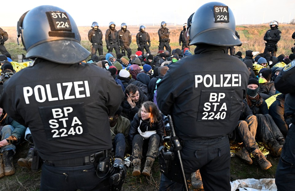 Police officers stand in front of a group of protesters - including Greta