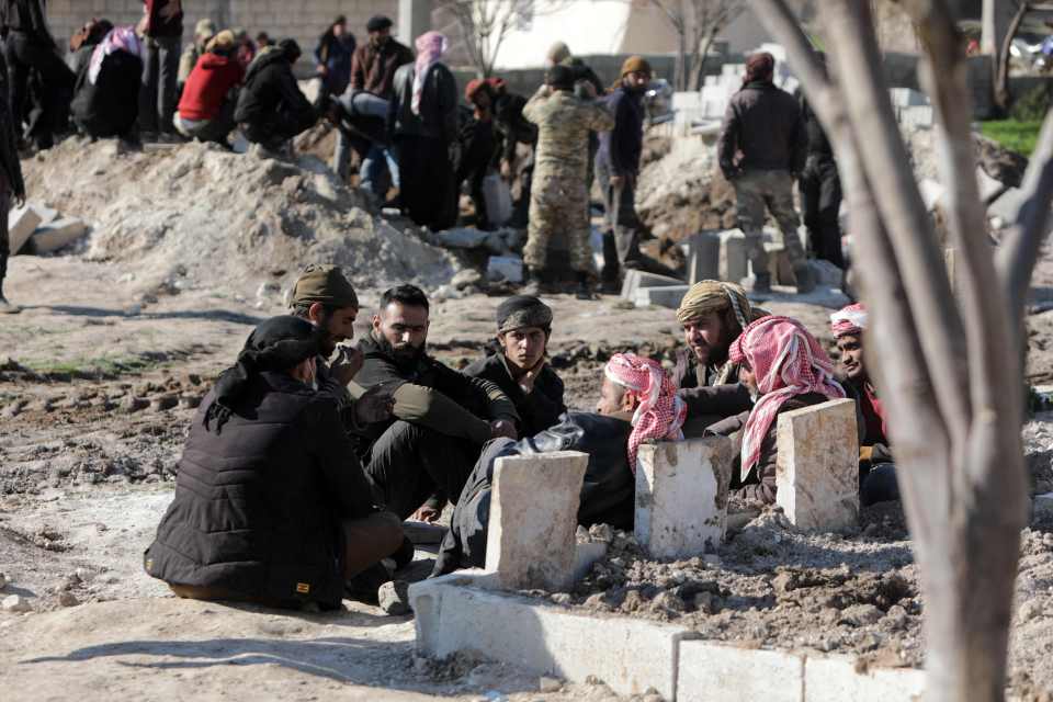 People gather around recently-dug graves to mourn the loss of their relatives