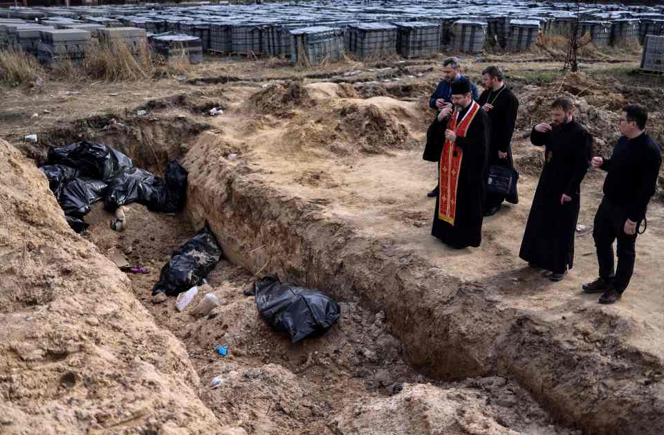 Priests pray by body bags in a mass grave in Bucha