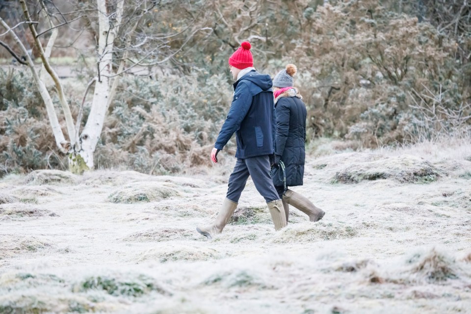 People walk through a frost covered field in Barnes Common, South West London this morning