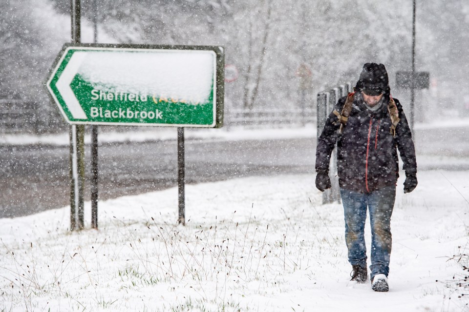 A man walks through heavy snow by a road sign at Chapel en le Frith, Derbyshire