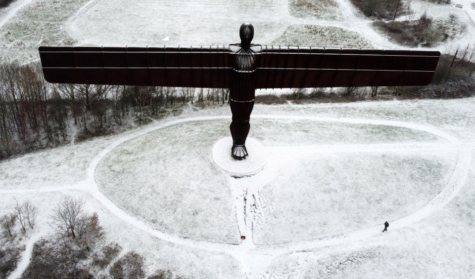 A man walks past the Angel of North after snowfall in Gateshead