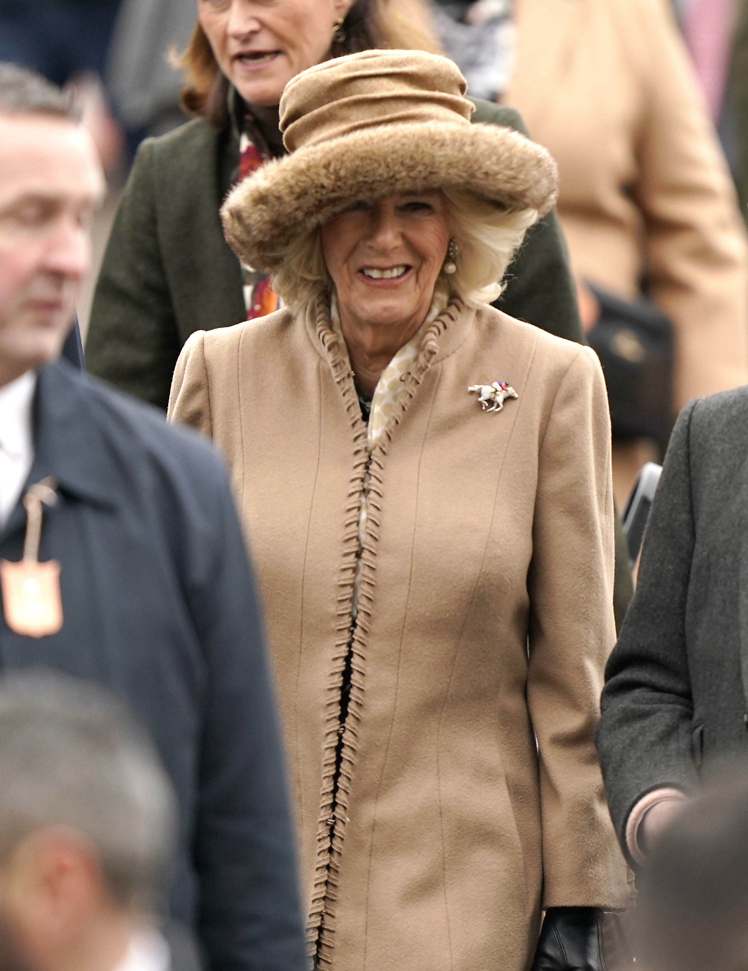 The Queen Consort arrives on day two of the Cheltenham Festival at Cheltenham Racecourse wearing a camel-coloured coat and matching hat