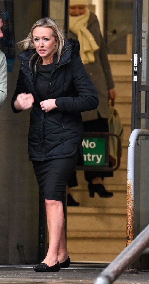 a woman in a black coat stands in front of a no entry sign