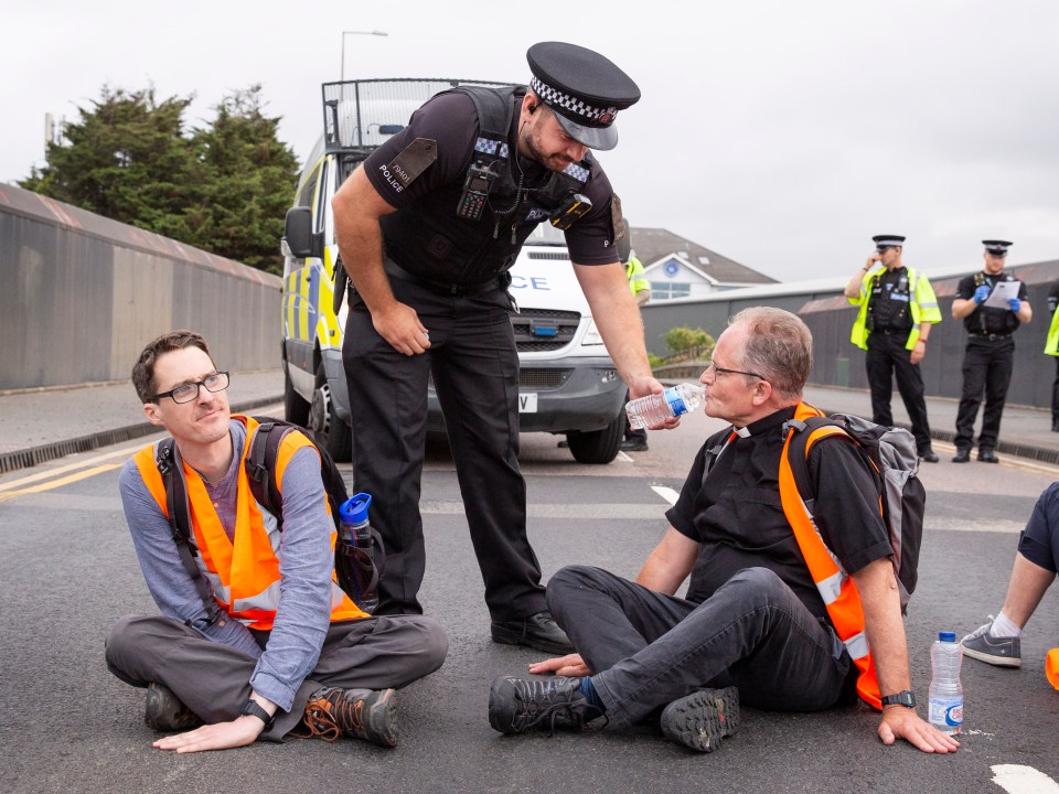 A police officer helps hydrate an eco-loon who glued himself to the road